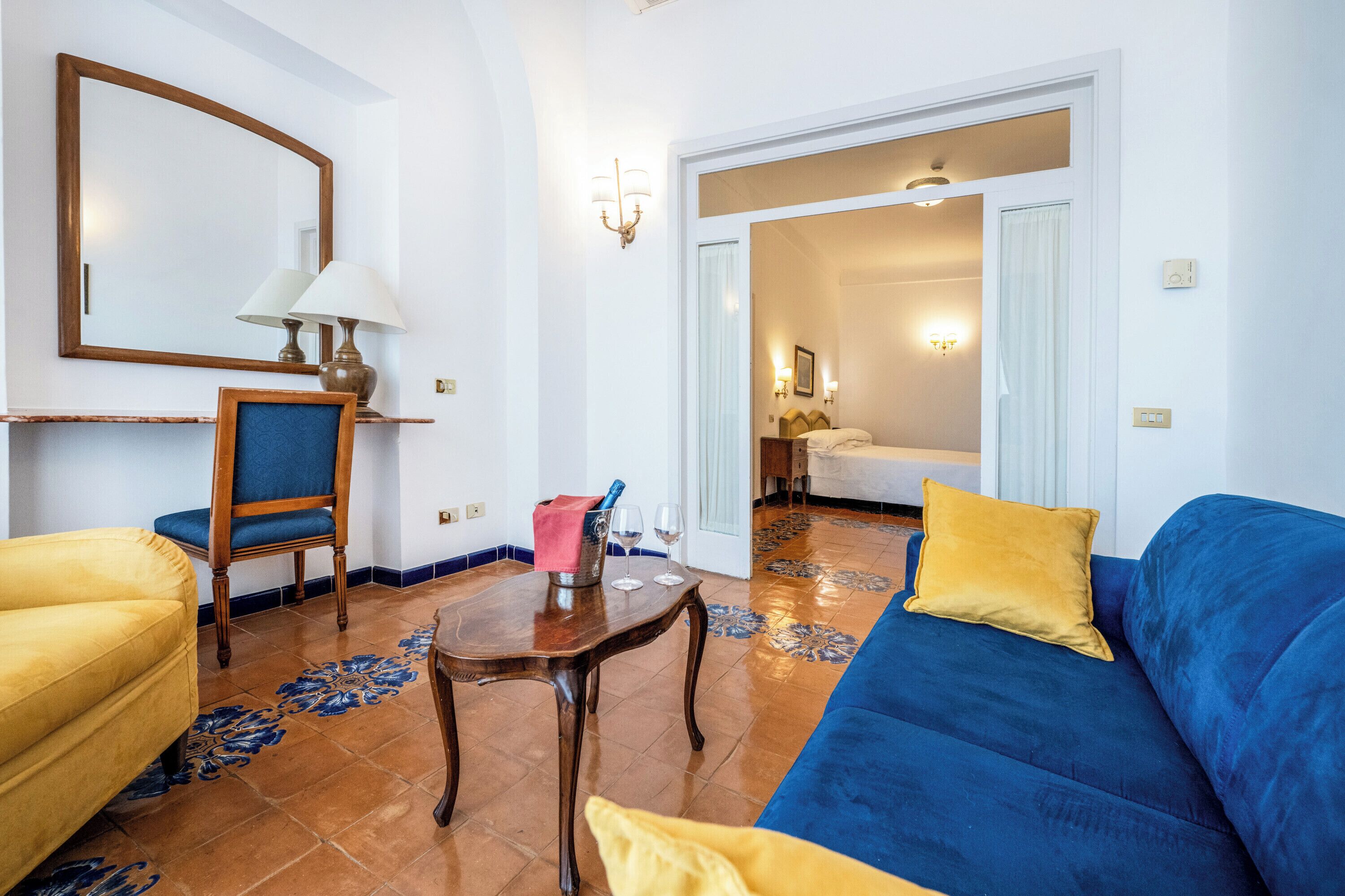 Uma sala de estar com um sofá azul, uma poltrona amarela, uma mesa de madeira e um espelho na parede.