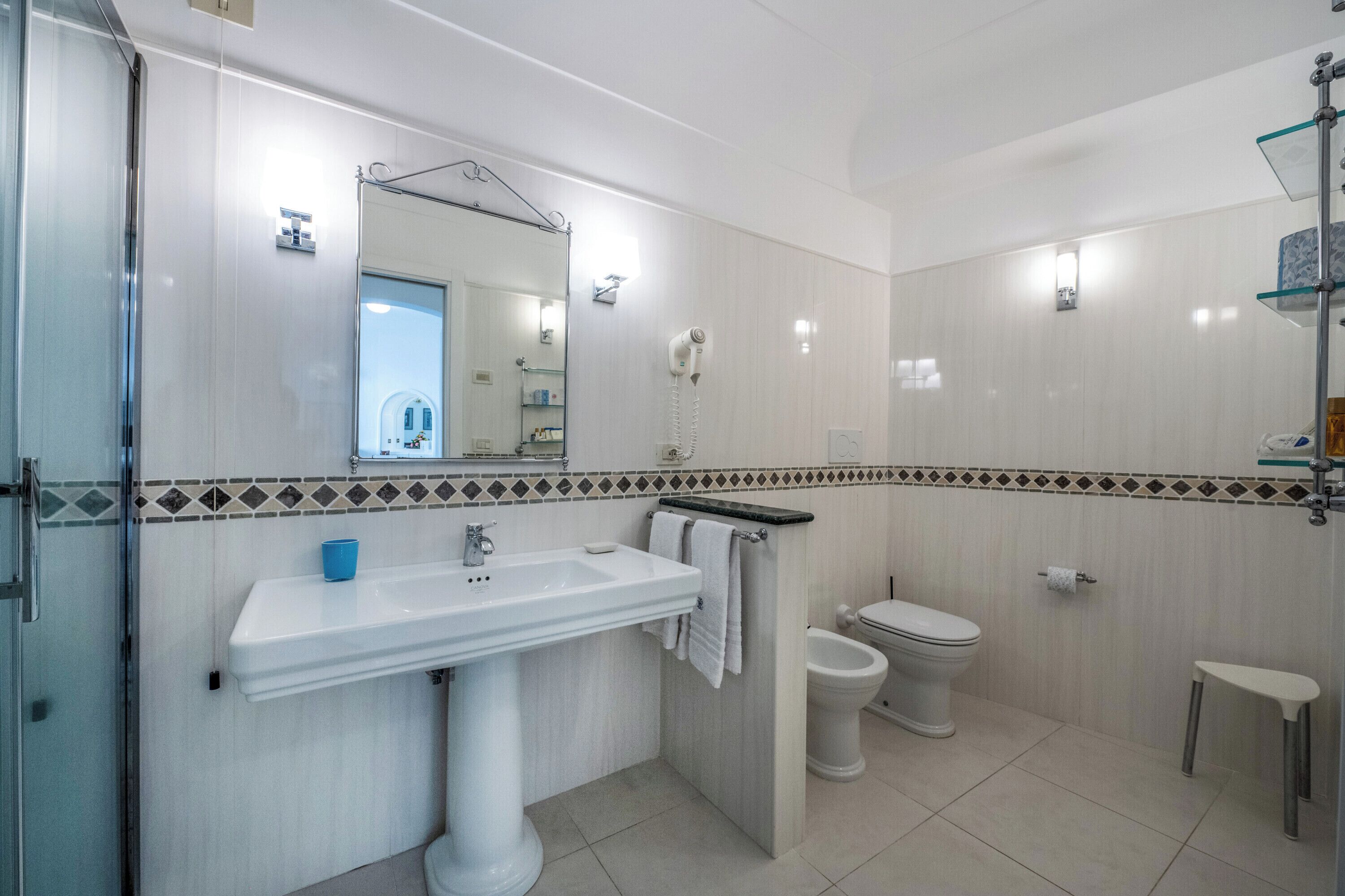 A modern bathroom with a white sink, a mirror, a toilet, and a shower area.
