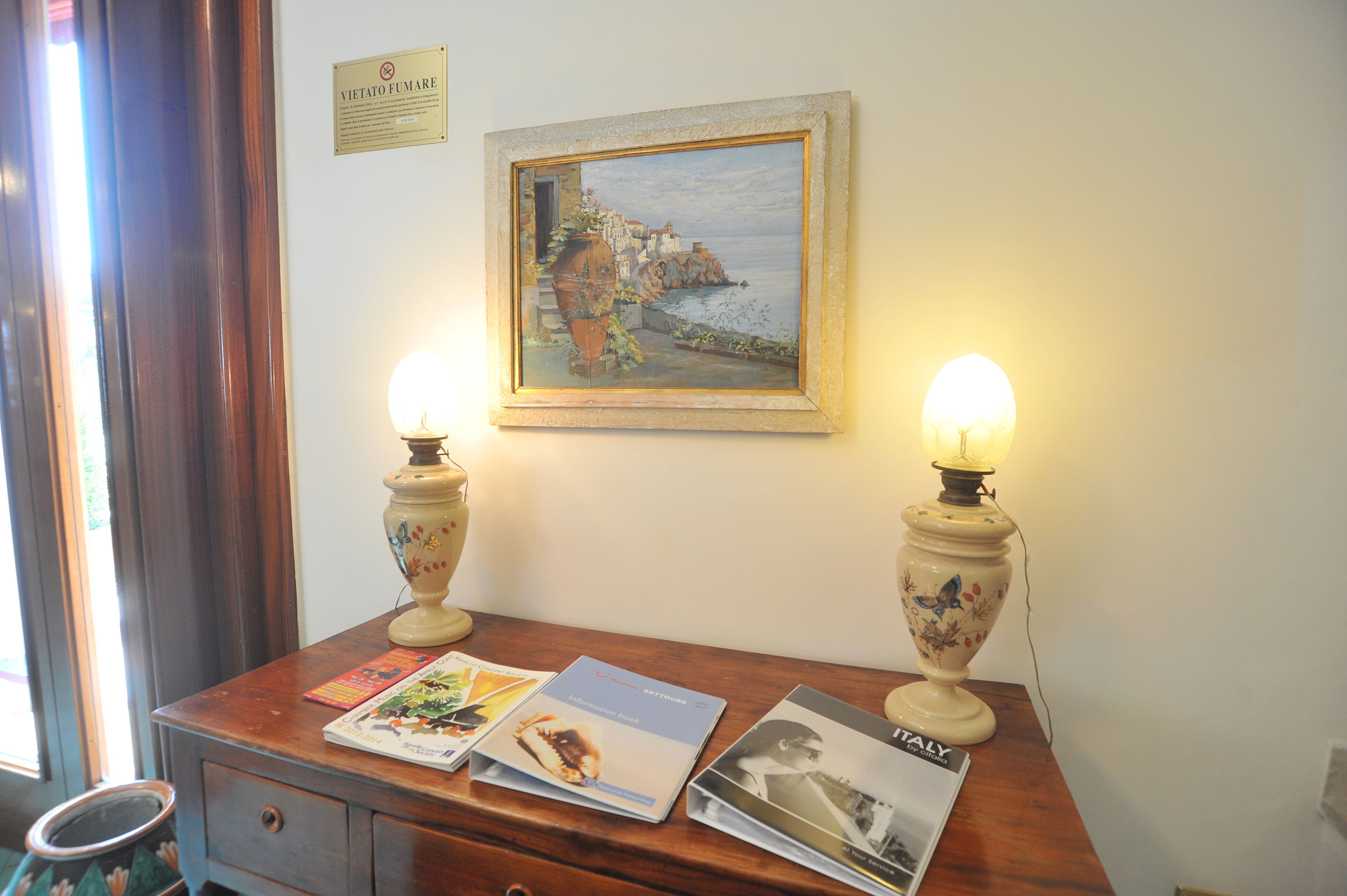 A wooden desk with two table lamps, a framed painting, and several travel brochures.