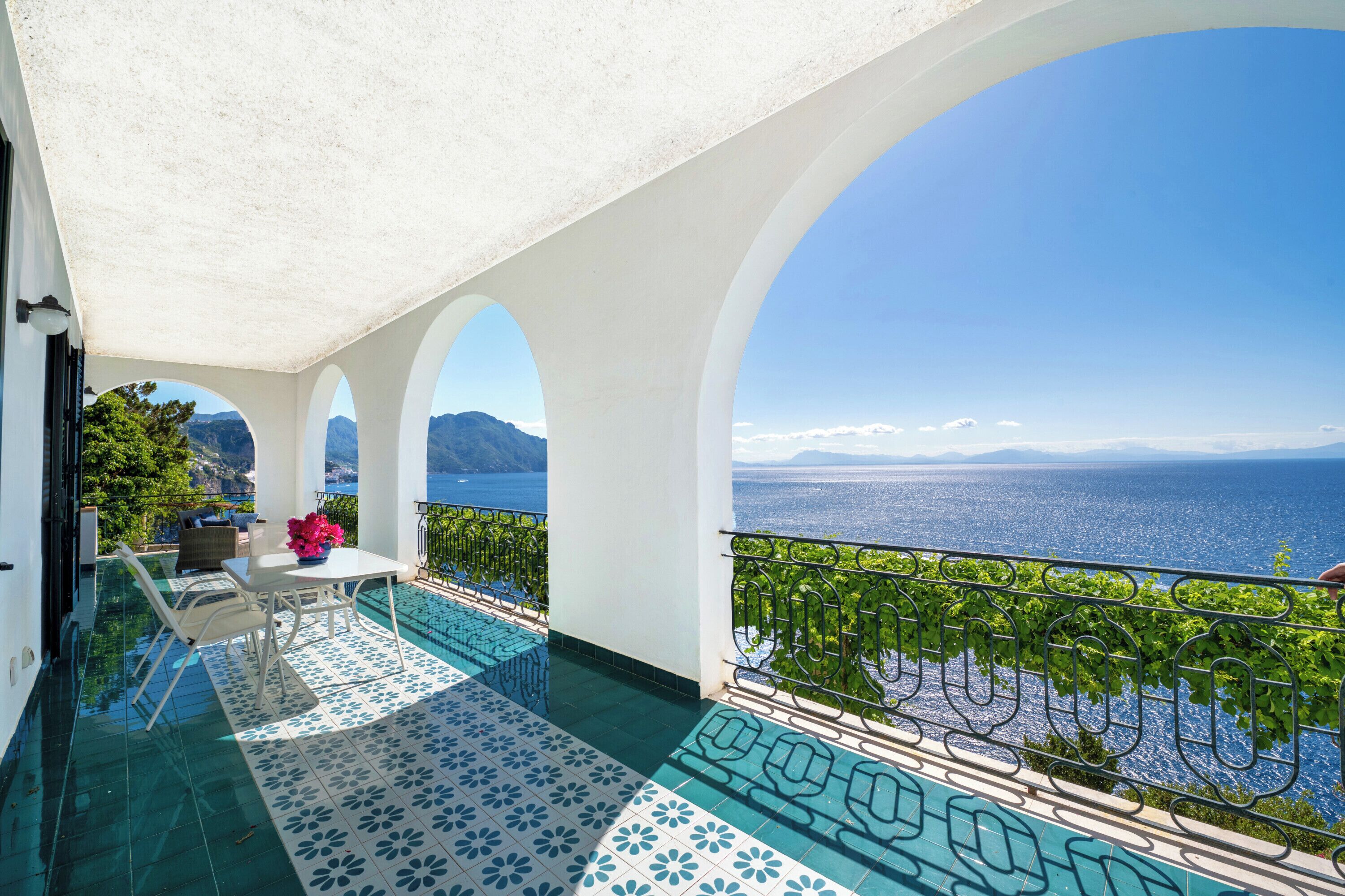 A balcony with a view of the sea, a tiled floor, and a table with chairs.