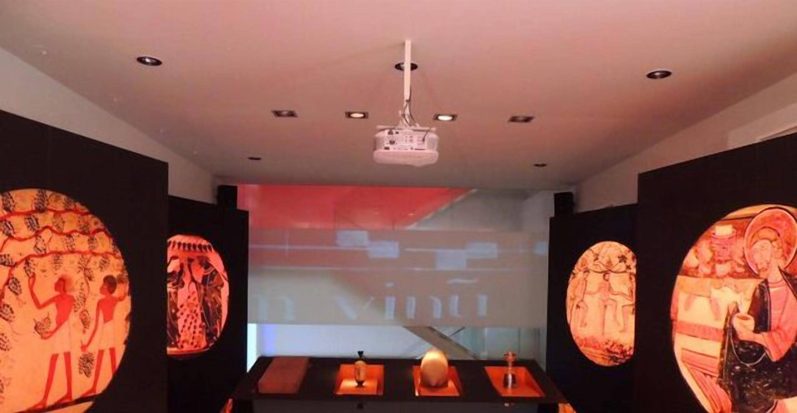 Un interior modern amb pantalla de projector, taula amb espelmes i decoració mural.