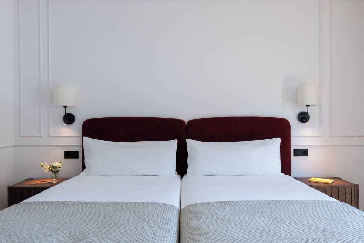 A double bed with a red headboard, white linens, and two bedside lamps.