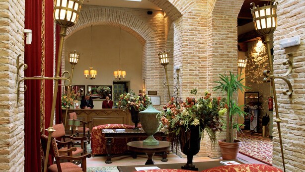 A lobby with brick walls, a reception desk, seating area, and decorative lighting. - Parador de Olite (Olite)