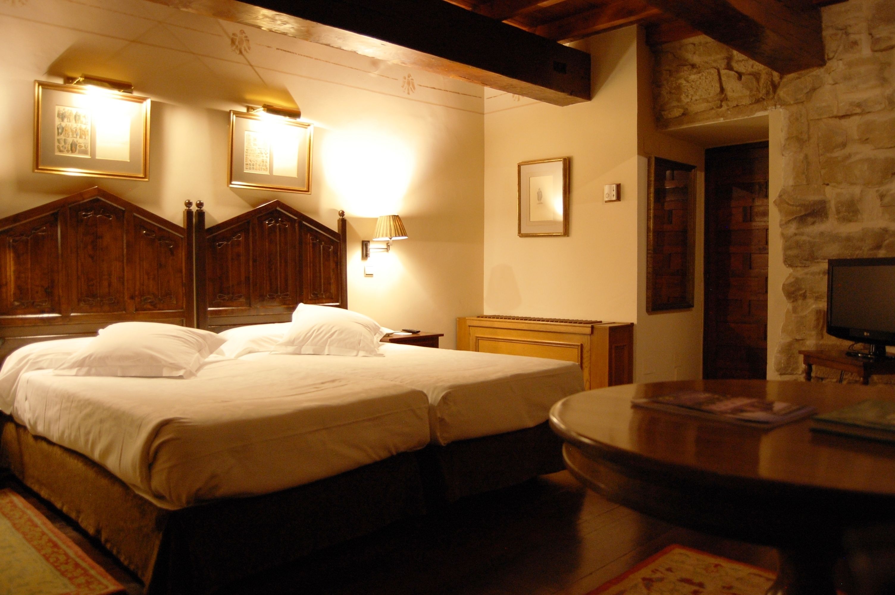 A hotel room with a large bed, wooden headboard, a television, and a stone wall.