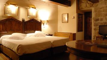 A hotel room with a large bed, wooden headboard, a television, and a stone wall.