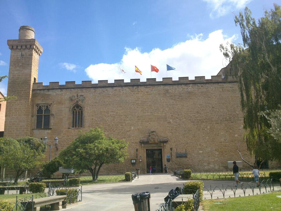 Un edificio histórico con una torre destacada, una entrada amplia y banderas en la parte superior.