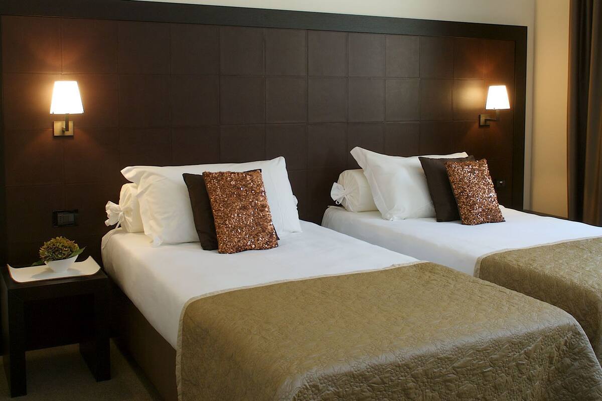 A hotel room with two beds, each with a headboard, bedside tables, and lamps.