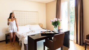 Una habitación de hotel con cama, una mesa de comedor con desayuno, un jarrón con flores y vistas al exterior.