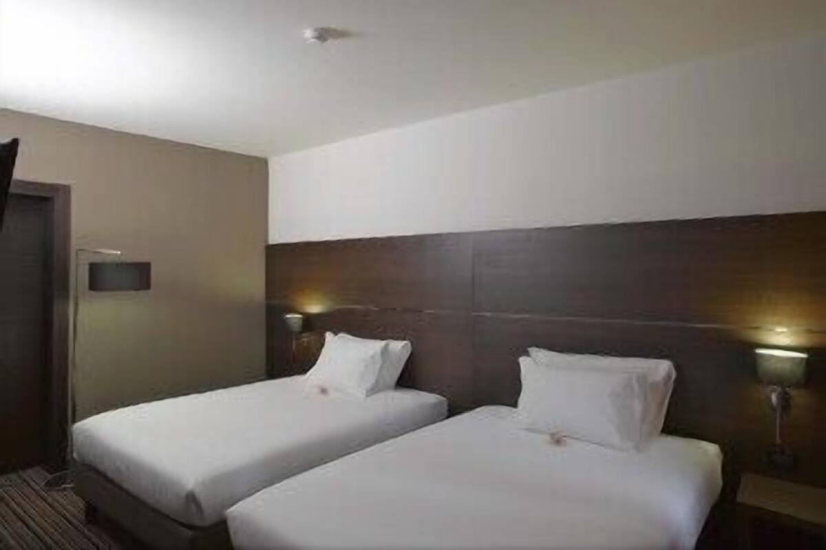 A hotel room with two single beds, a wooden headboard, bedside lamps, and a small nightstand.
