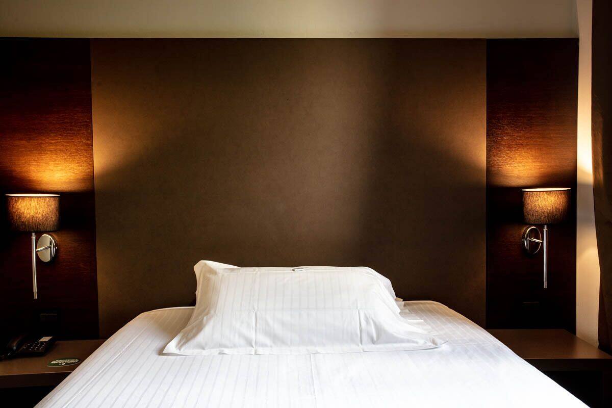 A hotel room with a neatly made bed, two bedside lamps, and a telephone on the nightstand.