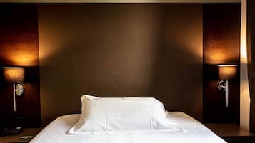 Quarto de hotel com cama bem arrumada, duas luminárias laterais e telefone na mesa de cabeceira.