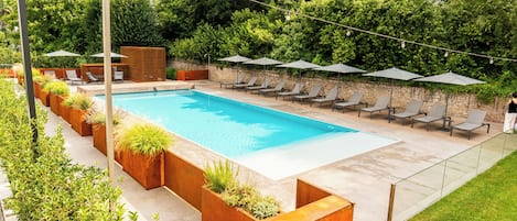 A rectangular swimming pool with lounge chairs and umbrellas, surrounded by planters and a grassy area.