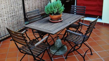 A patio with a wooden table and metal chairs, a potted plant, and a red awning.