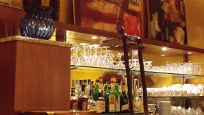 Un espace bar avec un comptoir, des verres, des bouteilles et un grand tableau abstrait accroché au mur.