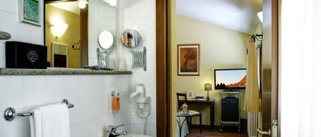 A hotel bathroom with a sink, mirror, towel rack, and a view of the room.