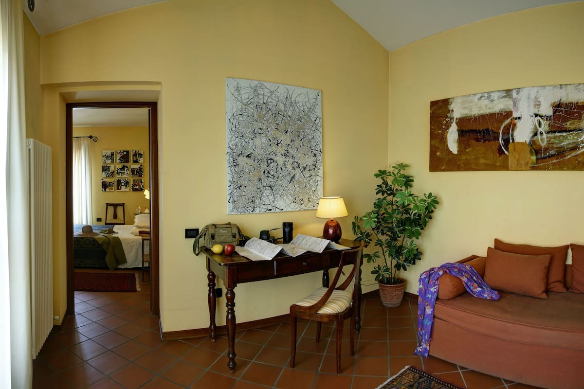 Ein gemütliches Wohnzimmer mit einer Couch, einem Tisch mit Lampe, einer Topfpflanze und einer Wand mit Kunstwerken.