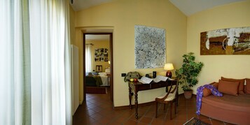 A cozy living room with a sofa, a table with a lamp, a potted plant, and a wall with artwork.