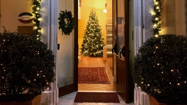 L’entrée d’un hôtel, avec un sapin de Noël, une enseigne indiquant « HÔTEL de PRATI » et le chiffre « 5 » peint sur le mur.