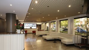 Un vestíbulo moderno con mostrador de recepción, zona de estar y amplios ventanales con vistas a la calle.