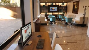 Un vestíbulo moderno con un mostrador de recepción de madera, una computadora y una pantalla de televisión. Varias zonas de estar con sillas blancas y azules.