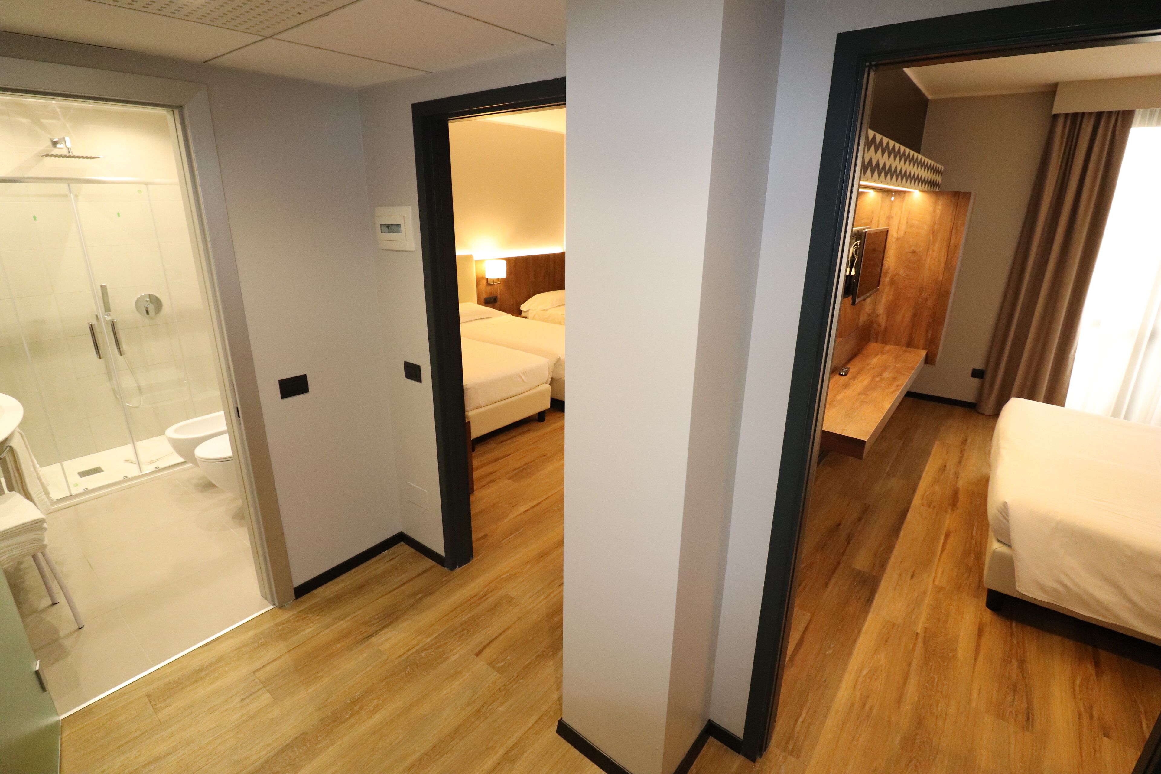 A hotel room with a wooden floor, a bed, a bathroom with a shower, and a small sitting area.