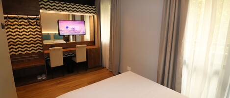Una habitación de hotel con cama, escritorio con computadora, televisor y zona de ducha.