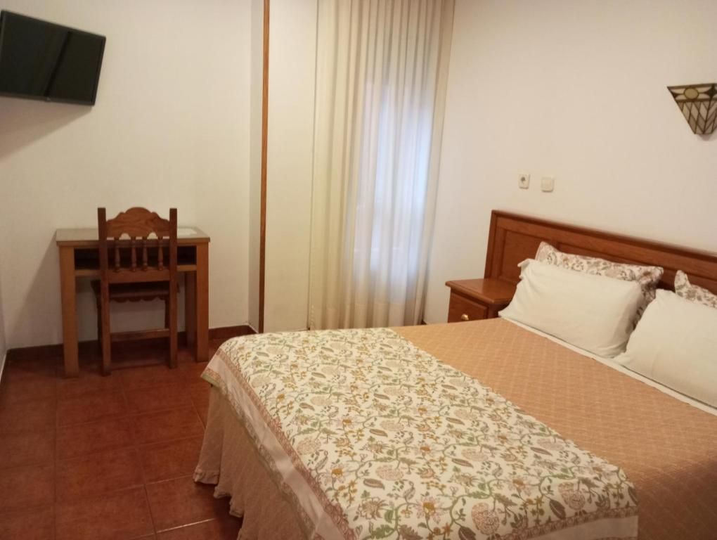 Ein Schlafzimmer mit einem Bett, einem Sessel, einem Nachttisch, einem an der Wand befestigten Fernseher und einem Fenster mit Vorhängen.