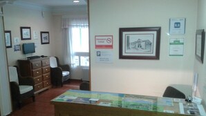 A reception area with a wooden desk, chairs, a television, framed pictures, and a 'No Smoking' sign. - Hospedaje Magallanes (Santander)