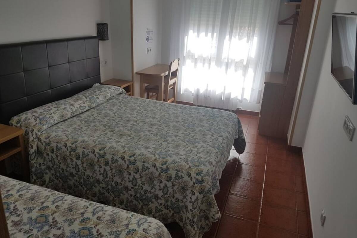 Une chambre avec deux lits, une petite table, une chaise, un téléviseur et une fenêtre avec des rideaux.