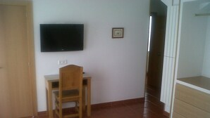 A room with a wooden chair, a television mounted on the wall, and a tiled floor. - Hospedaje Magallanes (Santander)