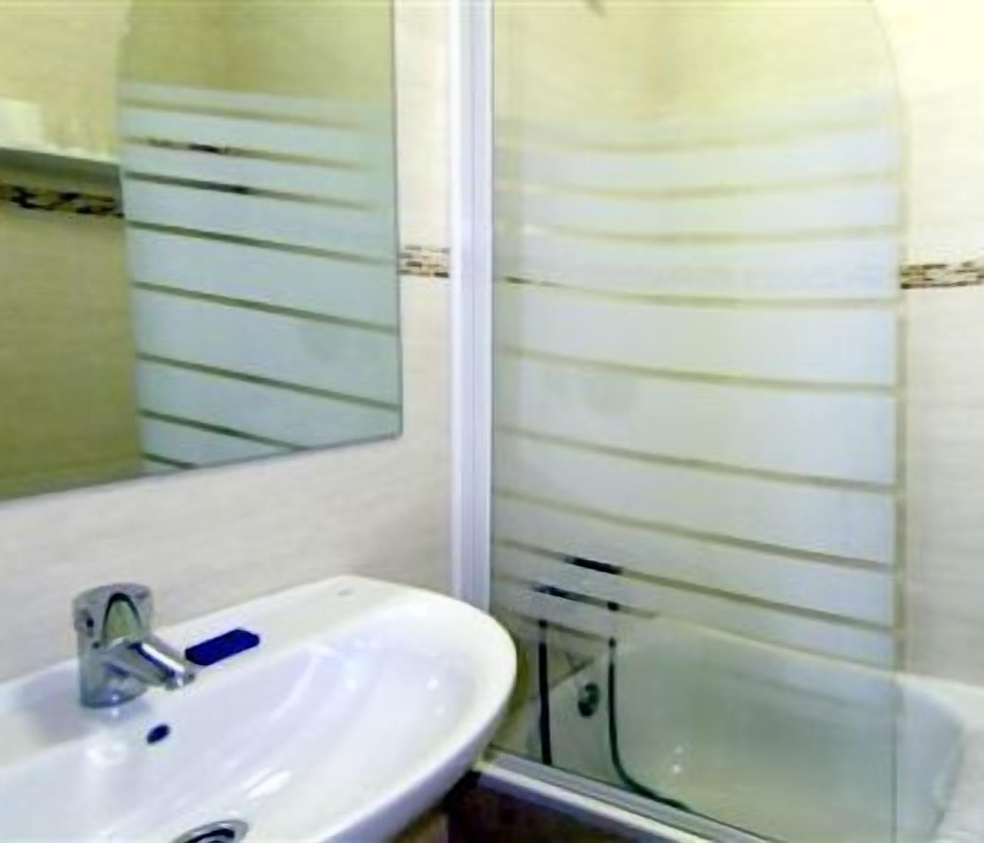 Een badkamer met een witte wastafel, een spiegel en een douchecabine met glazen wanden.