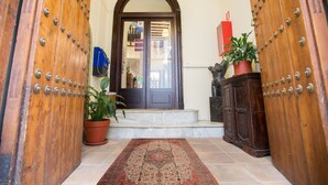 Una puerta de madera con remaches metálicos, una planta en maceta y un tapete que conduce a una escalera.
