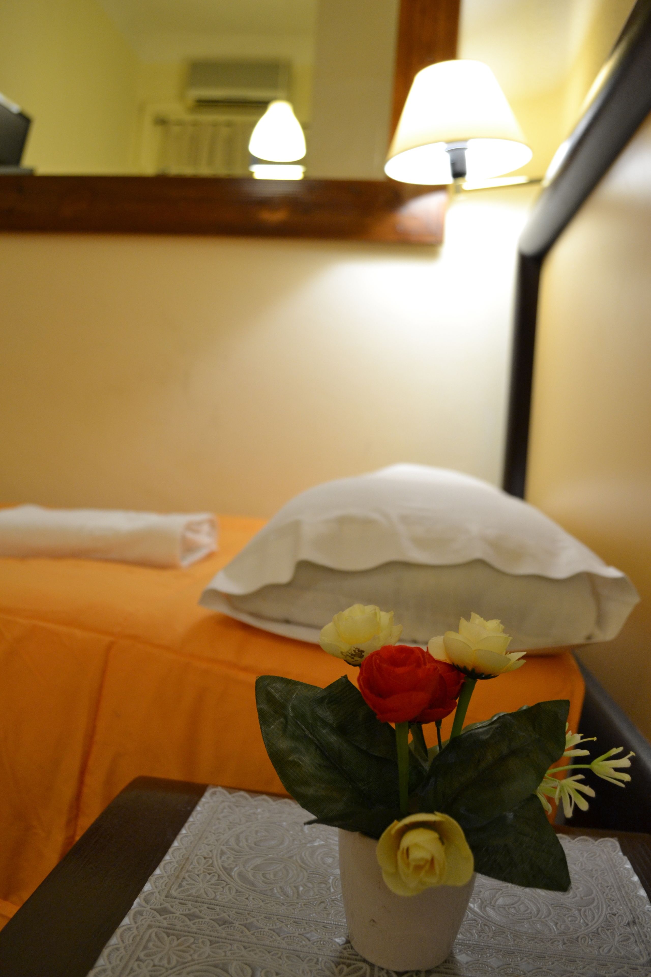 Ein Hotelzimmer mit einem Bett, einem Nachttisch mit Blumenvase und einer Lampe.