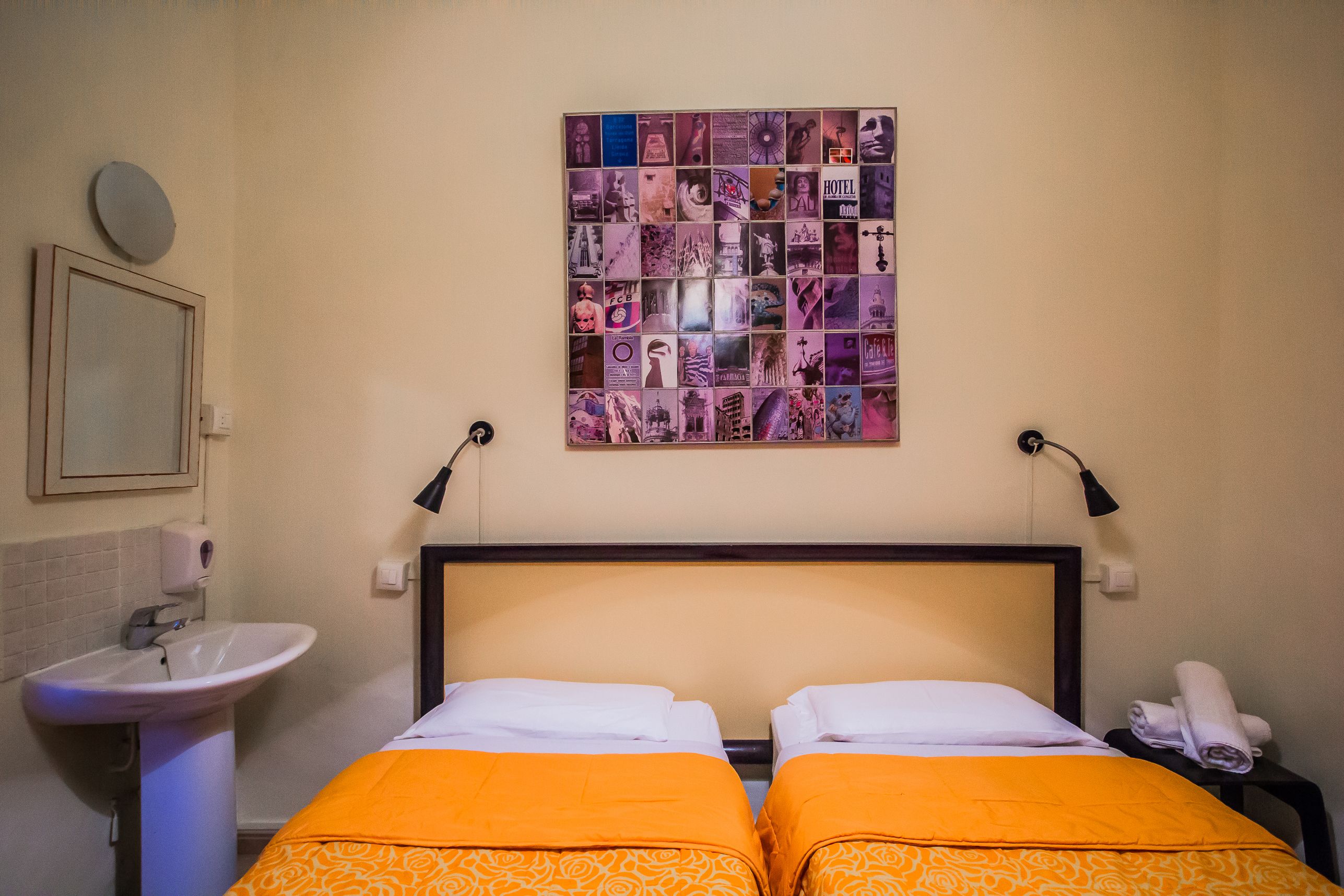A hotel room with two beds, a sink, a mirror, and a wall art collage.