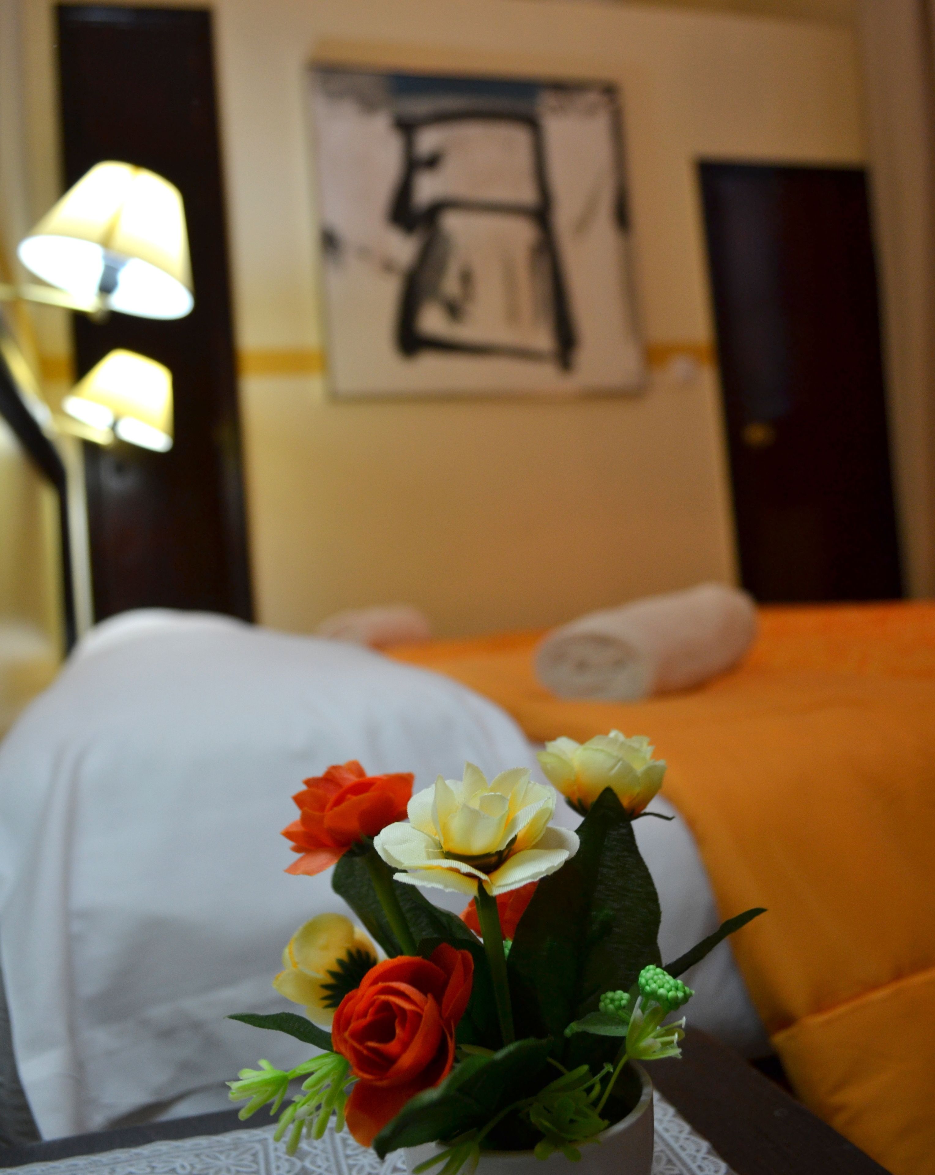 A hotel room with a bed, a nightstand with a vase of flowers, and a painting on the wall.