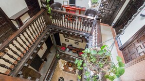 Un interior de varios niveles con una escalera de madera, un comedor con sillas rojas y una planta colgante.