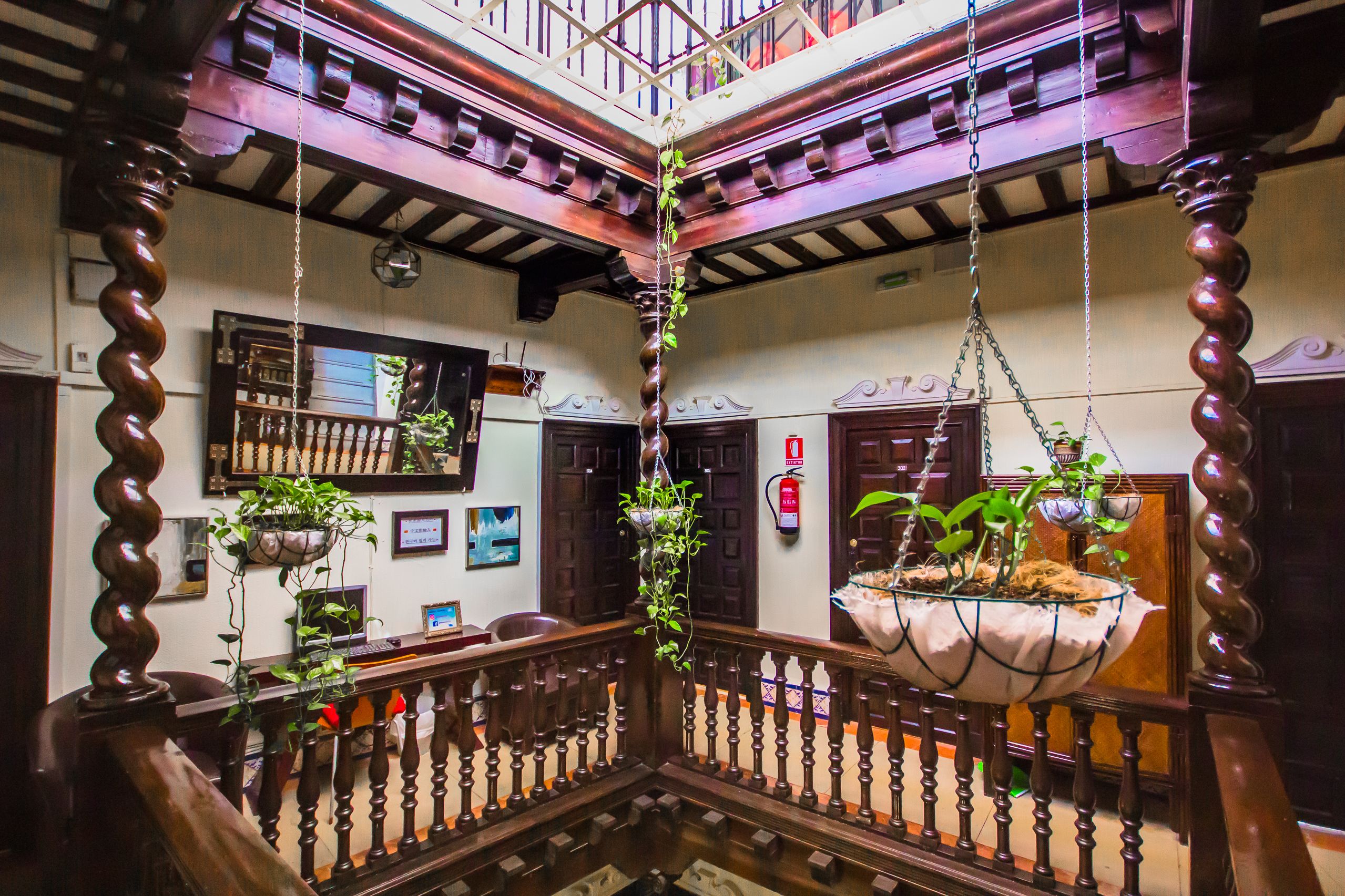 A traditional interior with a wooden staircase, hanging plants, and a balcony with a view.