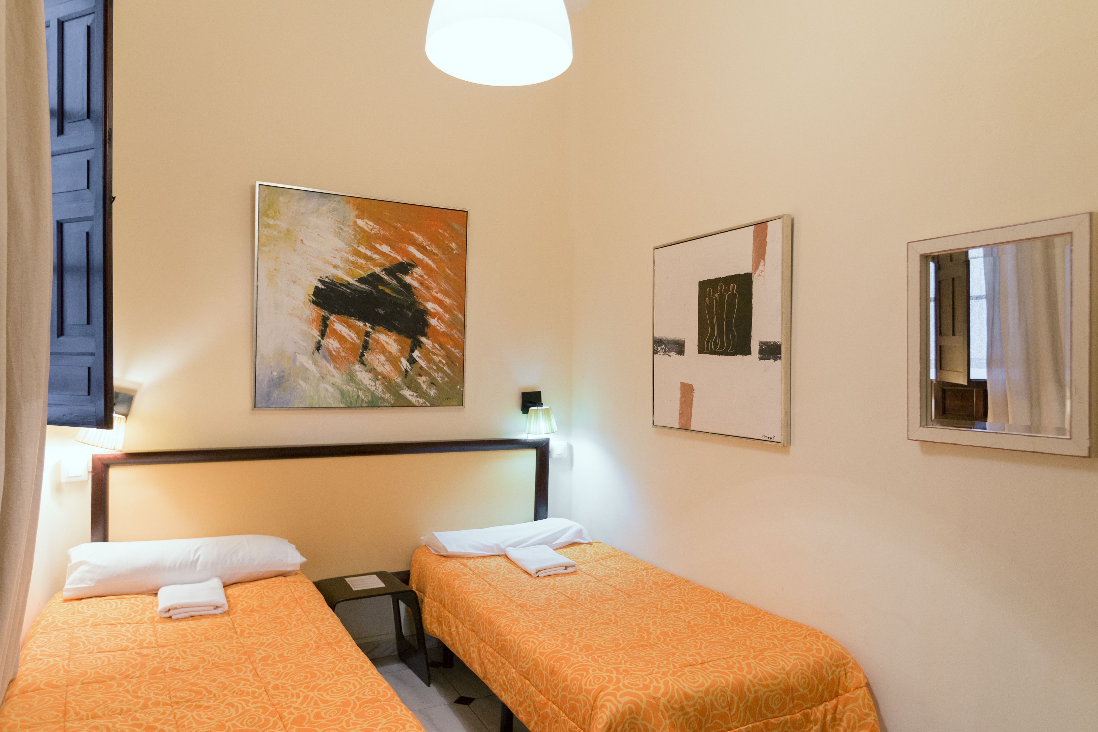 Ein Hotelzimmer mit zwei Einzelbetten, einem Nachttisch, einer Lampe und Bildern an den Wänden.