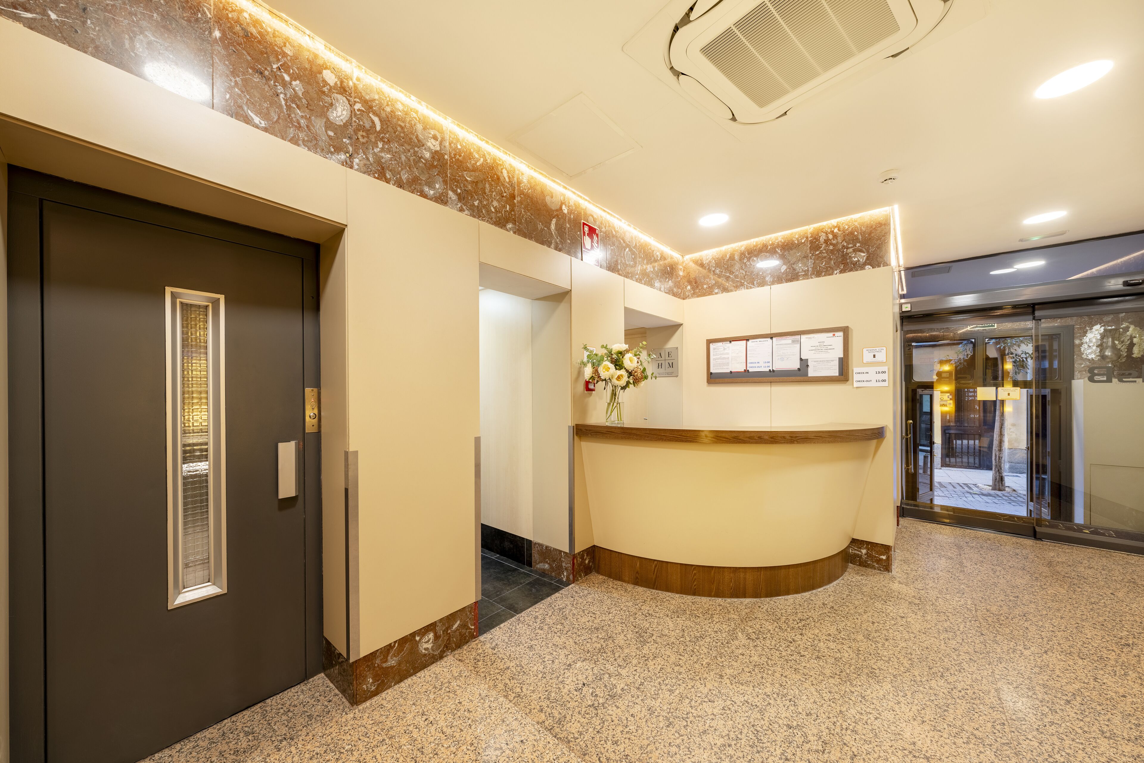 A reception area with a marble floor, a reception desk, a wall-mounted information board, and a door with a window.