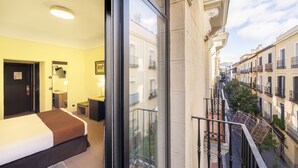 A hotel room with a large bed, a desk, and a balcony with a view of the street. - Hostal Ballesta (Madrid)