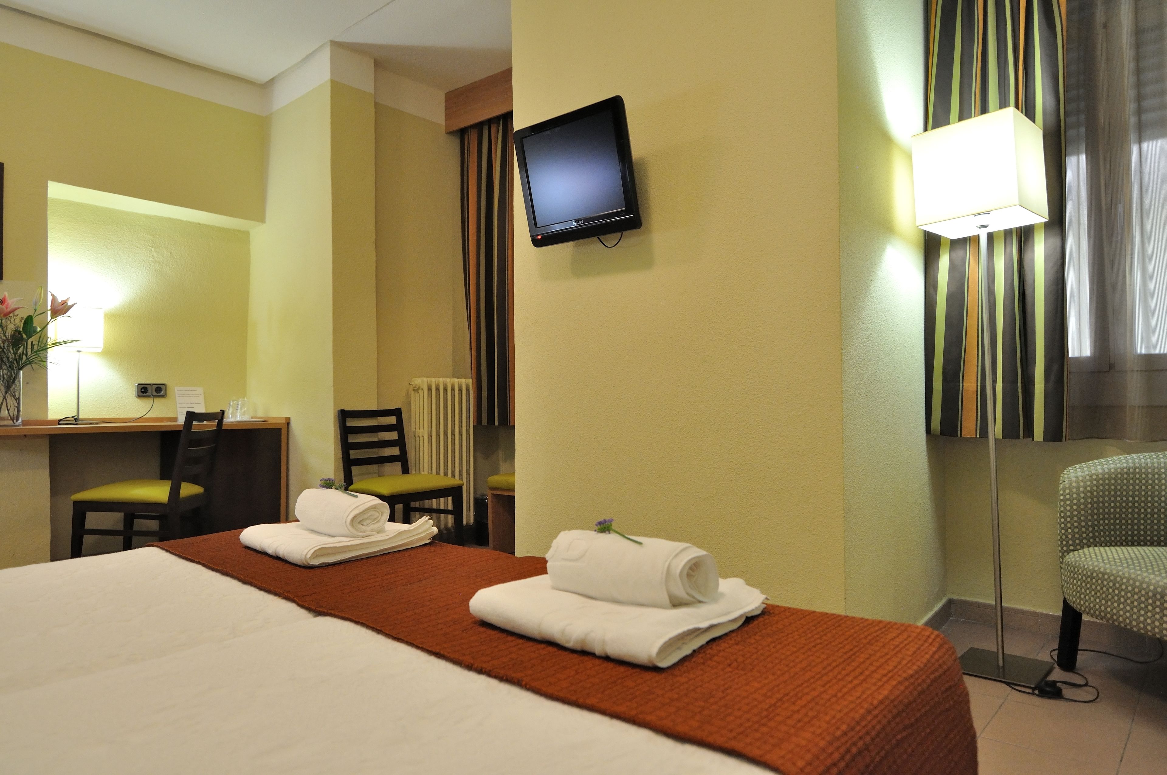 Una habitación de hotel con cama, escritorio, silla, televisión y lámpara.