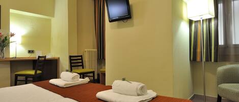 Una habitación de hotel con cama, escritorio, silla, televisión y lámpara.