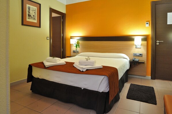 A hotel room with a bed, a nightstand, a wall-mounted lamp, and a door.