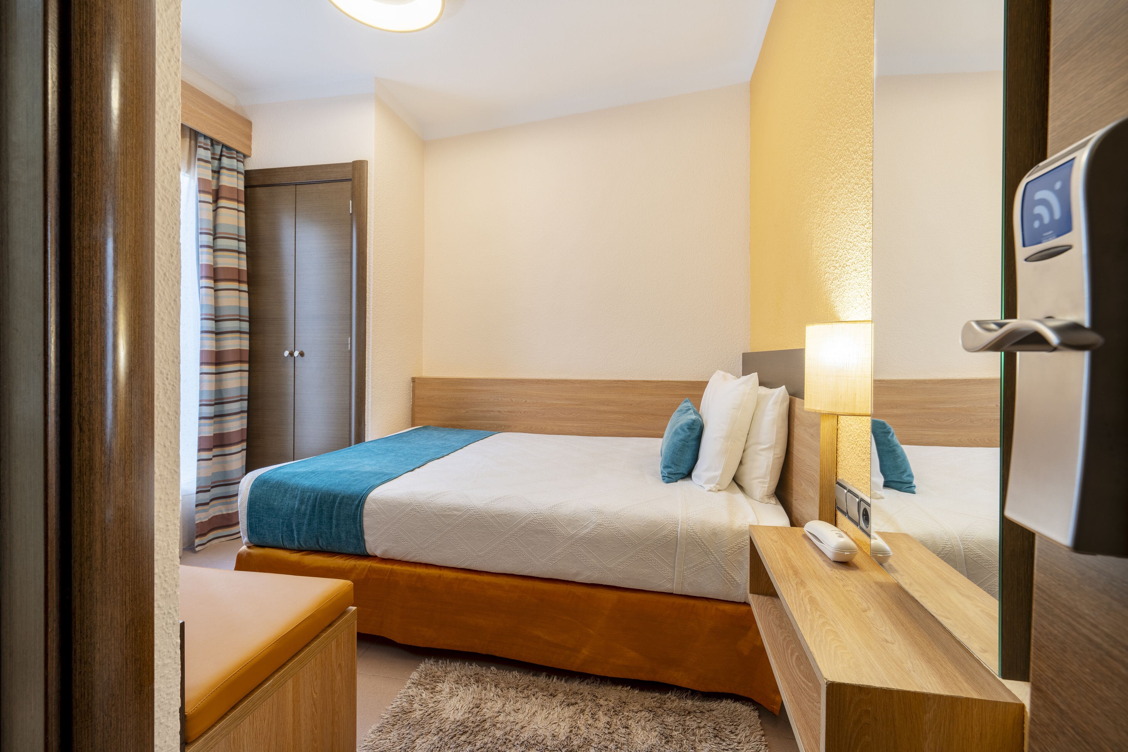 A hotel room with a bed, bedside table, lamp, and a mirror.