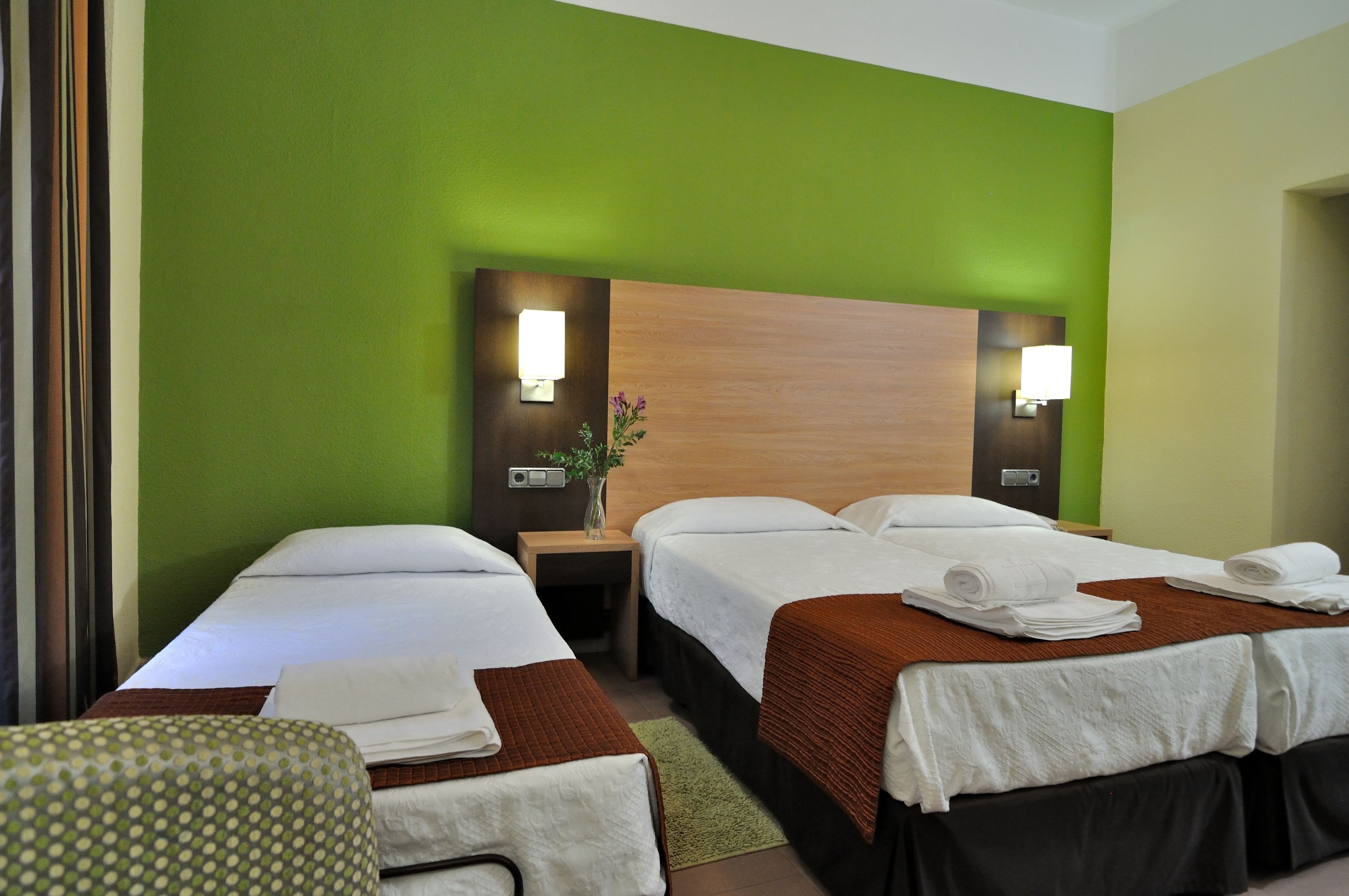 Ein Hotelzimmer mit zwei Betten, einem Nachttisch mit Lampe und einer grünen Wand.