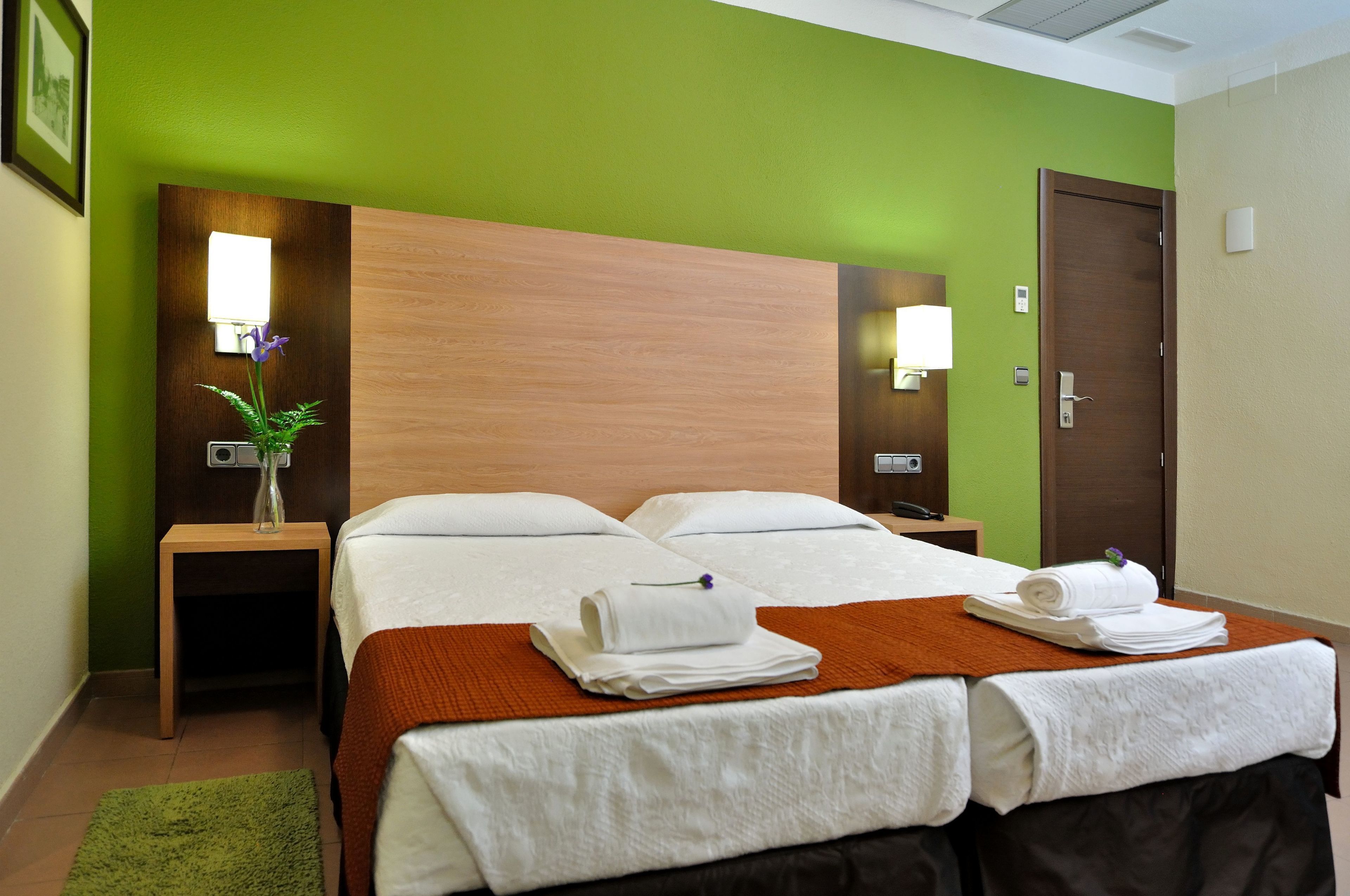 Ein Hotelzimmer mit einem großen Bett, zwei Nachttischen, einer grünen Wand und einem hölzernen Kopfteil.