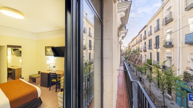 A hotel room with a bed, desk, chair, and a view of the street. - Hostal Ballesta (Madrid)