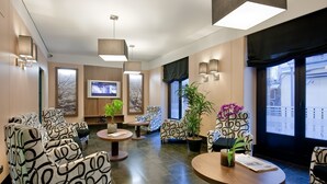 A modern lobby with patterned sofas, a TV, and potted plants. - Hostal Ballesta (Madrid)