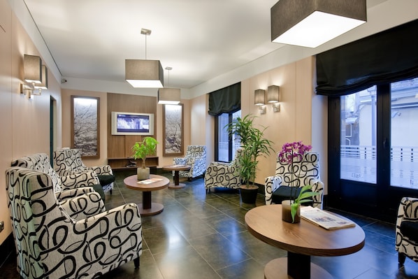 A modern lobby with patterned sofas, a TV, and potted plants. - Hostal Ballesta (Madrid)