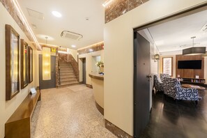 A hotel lobby with a reception desk, a staircase, and a seating area with patterned upholstery. - Hostal Ballesta (Madrid)